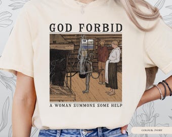 Puede incluir: Camiseta de color marfil con una ilustración de estilo vintage. El texto "GOD FORBID" está encima de la imagen y "A WOMAN SUMMONS SOME HELP" debajo. La imagen muestra figuras en un entorno rústico. Parte de la "WITCH PLEASE SERIES".