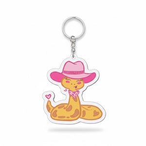 May include: A novelty keychain featuring a cartoon snake wearing a pink cowboy hat and bandana. The snake is yellow with brown spots and a pink heart. The keychain has a silver metal ring.