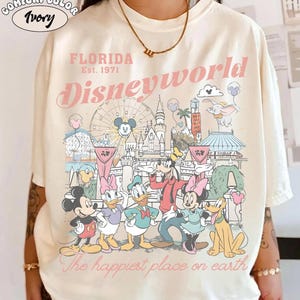 Peut inclure: T-shirt ivoire Comfort Color avec un motif de Disney World. Le design comprend le texte "FLORIDA Est. 1971 Disneyworld" et la phrase "The happiest place on earth". Mickey, Minnie, Donald et Dingo sont &eacute;galement repr&eacute;sent&eacute;s.