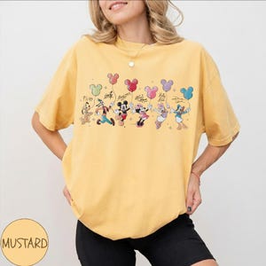 Może przedstawiać: Musztardowa koszulka z grafiką postaci Disneya trzymających balony w kształcie balon&oacute;w. Postacie to między innymi Pluto, Goofy, Myszka Miki, Myszka Minnie, Kaczka Daisy i Kaczor Donald. Koszulka ma okrągły dekolt i kr&oacute;tkie rękawy.
