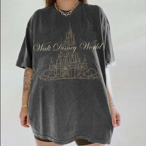 K&ouml;nnte beinhalten: Dunkelgraues T-Shirt mit dem Schriftzug "Walt Disney World" und einer Schlossillustration. Das Design hat einen verblichenen Vintage-Look. Das Shirt hat kurze &Auml;rmel und eine lockere Passform.