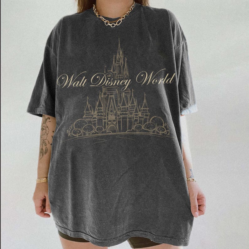 K&ouml;nnte beinhalten: Dunkelgraues T-Shirt mit dem Schriftzug "Walt Disney World" und einer Schlossillustration. Das Design hat einen verblichenen Vintage-Look. Das Shirt hat kurze &Auml;rmel und eine lockere Passform.