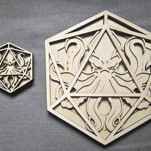May include: Two light-colored wooden wall art pieces shaped like twenty-sided dice, each featuring a laser-cut design of a multi-tentacled creature inside the geometric frame. The wood has a natural, smooth finish with visible grain patterns.