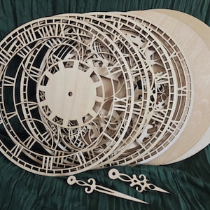 Peut inclure: Plusieurs faces d'horloge en bois non finies et des aiguilles d'horloge. Les faces d'horloge présentent des motifs découpés complexes avec des chiffres romains et des éléments décoratifs. Les aiguilles ont un design pointu et décoratif. Les articles sont en bois clair.