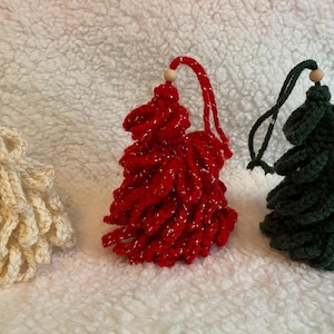 May include: Three handmade Christmas tree ornaments. One is cream-colored, one is red with silver glitter, and one is dark green. Each tree has a loop for hanging and a small wooden bead at the top. The ornaments are made of yarn.