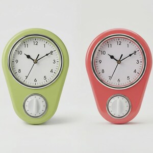 Könnte beinhalten: Zwei Küchenuhren im Retro-Stil. Eine ist hellgrün, die andere korallenfarben. Beide haben weiße Zifferblätter mit schwarzen Zahlen und Zeigern sowie ein kleines Timer-Zifferblatt darunter. Auf weißem Hintergrund.