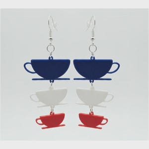 May include: A pair of dangle earrings featuring a vertical stack of three tea cup charms in blue, white, and red. Each earring hangs from a silver-toned metal hook and includes three connected cup shapes, with the blue cup at the top, white in the middle, and red at the bottom.