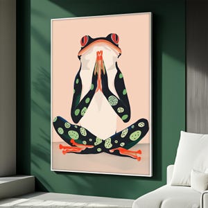 Puede incluir: Una impresión artística enmarcada que presenta una rana estilizada en una postura de yoga. La rana tiene un cuerpo blanco, extremidades negras con lunares verdes y ojos rojos. El fondo es rosa claro y el marco es blanco.