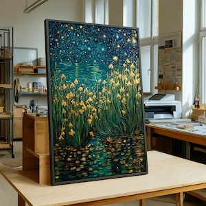 May include: Framed artwork depicting a nighttime waterscape with yellow flowers and green foliage. The painting features a dark blue sky with golden stars and a reflective water surface. The artwork is displayed on a wooden table in a well-lit studio.