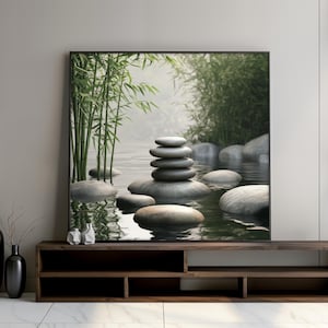 Op de afbeelding: Een ingelijste print met een serene zen-tuin. Gladde, grijze stenen zijn opgestapeld in een toren in het water, omringd door andere stenen en bamboestengels. Het water weerspiegelt de scène, wat een gevoel van rust creëert.
