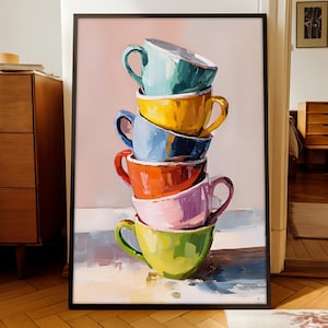 Op de afbeelding: Een ingelijste kunstdruk met een stapel kleurrijke theekopjes. De theekopjes zijn geschilderd in tinten blauw, geel, oranje, roze en groen. Het kunstwerk heeft een textuur, schilderachtige stijl, met zichtbare penseelstreken. De achtergrond is zachtroze.