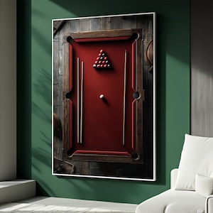 May include: A framed artwork featuring a red pool table with a wooden frame. The table is set with a rack of billiard balls and two cues. The background is a dark wood paneling.