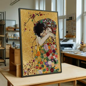 May include: Framed art print of Gustav Klimt's "The Kiss," featuring two embracing figures. The artwork showcases a gold background with floral and geometric patterns, and a black frame. The figures are adorned with colorful flowers.