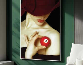 May include: A framed art print featuring a woman wearing a burgundy hat and holding a red billiard ball with the number 3. The woman's lips are painted red, and the background is black.