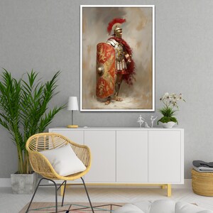 May include: A framed print of a Roman soldier in full armor, holding a shield. The soldier wears a red plume helmet, a red cape, and a detailed breastplate. The shield is red and gold with a detailed emblem. The artwork is displayed on a white cabinet.