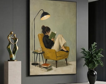 May include: A framed wall art print depicting a person with dark hair in a bun, wearing a black sweater and light-colored trousers, sitting in a mustard yellow armchair while reading a green book. A tall black floor lamp stands beside the chair.