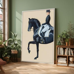 May include: A framed equestrian art print depicts a black horse in a dressage pose, ridden by a person in formal attire. The artwork features a cream-colored background and is displayed in a room with plants and a wooden bookshelf.