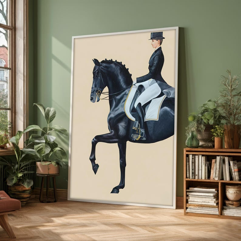 May include: A framed equestrian art print depicts a black horse in a dressage pose, ridden by a person in formal attire. The artwork features a cream-colored background and is displayed in a room with plants and a wooden bookshelf.