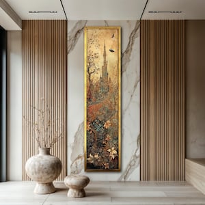 May include: Vertical framed artwork featuring a detailed landscape with a castle, trees, and flowers in warm tones. The artwork has a gold frame and is displayed on a marble and wood paneled wall. Two birds are flying in the sky.