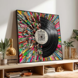 May include: A framed artwork featuring a black vinyl record with the text "ACIDMTH" on the label. The record is set against a backdrop of colourful book spines, creating a vibrant and artistic composition. The artwork is displayed on a wooden shelf.