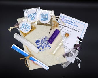 May include: A beige drawstring pouch with a blue logo, containing small plastic bags of dried elderflower, bay leaf, and thyme. Includes a white selenite wand, a purple textured candle, a glass vial, a small key, crystals, and an instruction card.