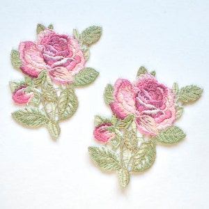 May include: Two embroidered floral patches featuring pink roses with green leaves. The patches have a detailed design with varying shades of pink and green. The patches are likely for decorative purposes, such as embellishing clothing or accessories.