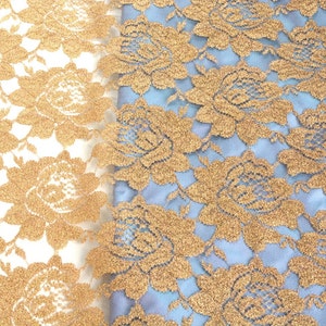 May include: Two pieces of gold lace fabric with a floral pattern. One piece is on a white background and the other is on a light blue background.