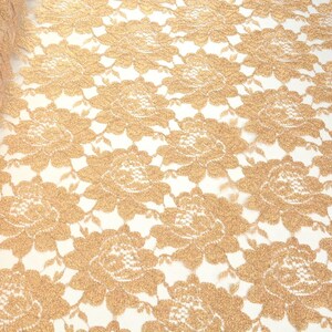 May include: Gold glitter lace fabric with a floral pattern. The lace is delicate and has a soft, shimmery finish.