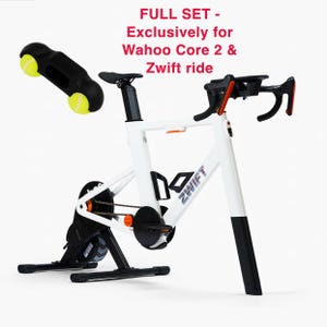 Op de afbeelding: Een witte Zwift-trainingsfiets met zwarte accenten en oranje details. De fiets heeft een zwart zadel en stuur. Een zwart accessoire met twee gele tennisballen is inbegrepen. De tekst op de afbeelding luidt "FULL SET - Exclusively for Wahoo Core 2 & Zwift ride."