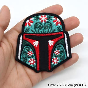 Puede incluir: Parche bordado con diseño de casco en negro, rojo, turquesa y blanco. El parche mide 7,2 x 8 cm. El diseño incorpora detalles florales y de volutas, con un panel central negro.