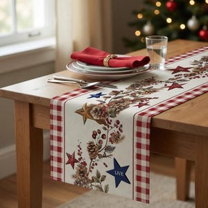 Puede incluir: Un camino de mesa crema con borde a cuadros rojo y blanco, decorado con estrellas rojas, piñas y bayas. Una servilleta roja, platos y cubiertos están colocados sobre una mesa de madera. La palabra "LIVE" está en una estrella azul.