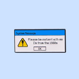 Op de afbeelding: Een rechthoekige emaille pin met een retro computerfoutmelding ontwerp. De pin heeft een blauwe bovenbalk met de tekst "System Message". De boodschap luidt "Please be patient with me, I'm from the 1900s" met een "OK" knop.