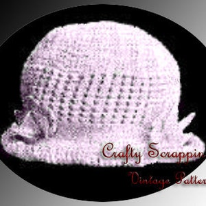 May include: A crocheted baby hat in a pale purple colour. The hat has a simple design with a small bow on the side.