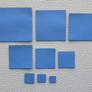 May include: An assortment of blue square leather patches in different sizes, displayed on a textured grey surface. The patches vary in size, highlighting the material's colour and texture.