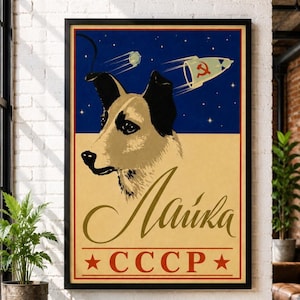 May include: A framed poster featuring a stylized illustration of the dog Laika against a dark blue starry sky and a cream background. A white rocket with a red hammer and sickle symbol flies above. The text reads Laika and CCCP with two red stars.