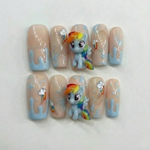 May include: Artificial nails with a light pink base and blue detailing. Each nail has a cloud and rainbow design, with two featuring a small, colourful pony figurine. The nails are designed for a fun and playful look, perfect for a whimsical style.