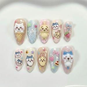 May include: A set of ten artificial nails with various cartoon character designs. The nails feature a variety of colors, including pink, blue, and yellow, and are decorated with 3D elements like bears, bunnies, and bows. The nails are arranged on a white surface.