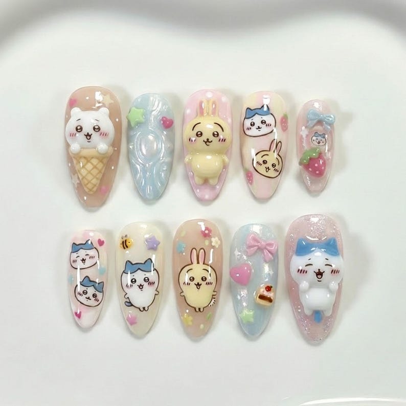May include: A set of ten artificial nails with various cartoon character designs. The nails feature a variety of colors, including pink, blue, and yellow, and are decorated with 3D elements like bears, bunnies, and bows. The nails are arranged on a white surface.
