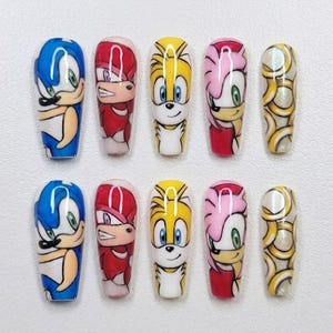 Può includere: Un set di dieci unghie finte con personaggi dei cartoni animati. Le unghie presentano Sonic the Hedgehog, Knuckles, Tails, Amy Rose e un design a spirale dorata. Ogni unghia è dipinta con colori vivaci e dettagliate illustrazioni dei personaggi.