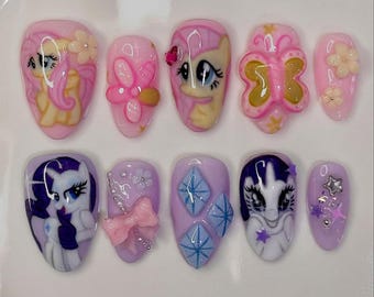 Puede incluir: Un conjunto de diez uñas artificiales con temática de dibujos animados. Las uñas presentan colores rosa, amarillo y morado con varios diseños, incluyendo mariposas, flores y personajes de dibujos animados. Algunas uñas tienen adornos 3D.