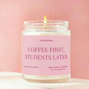 Może przedstawiać: Biały ceramiczny kubek z czarnym uchwytem i napisem "But First, Coffee" pogrubioną czcionką. Kubek jest ustawiony na rozmytym tle, sugerującym przytulne otoczenie.