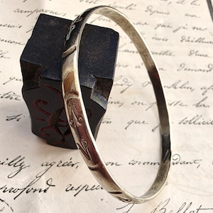 Peut inclure: Un bracelet jonc en métal argenté orné d'une série de motifs gravés répétitifs en forme de feuilles sur sa surface extérieure. Le bracelet présente une finition lisse et polie ainsi qu'un profil arrondi, témoignant d'un travail soigné.