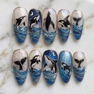 May include: A set of ten artificial nails, each decorated with a whale design. The nails depict orca whales in a blue ocean, with waves and a starry sky. The designs are in black, white, and blue.