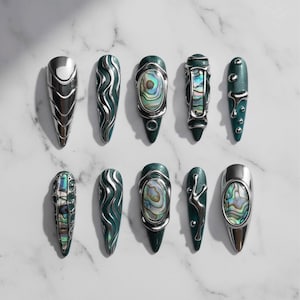 May include: An assortment of ten artificial nails in various designs. The nails feature a combination of silver metal and teal-green bases. Some nails have abalone shell accents, while others have wave or droplet designs.