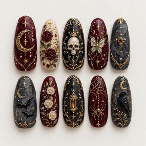 May include: A set of ten almond-shaped press-on nails featuring intricate 3D designs in gold, deep red, black, and cream. Motifs include a crescent moon, roses, a skull with a crown, a butterfly, a cross, bats, a lantern, a spider, and a raven.
