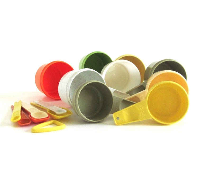 May include: A set of vintage measuring cups in various colors, including green, orange, white, and yellow. The cups are made of plastic and have a speckled finish. The set includes a variety of sizes, including 1/4 cup, 1/2 cup, 1 cup, and 2 cups.