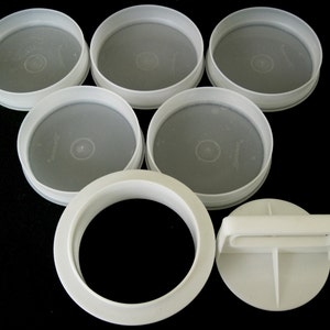 May include: Set of six white plastic burger patty moulds. The moulds are round and have a raised edge. There is also a separate white plastic press with a handle.