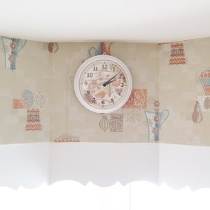 Peut inclure: Une horloge blanche avec des aiguilles noires et des chiffres romains sur un mur beige &agrave; motif floral. L'horloge a un motif floral sur le cadran.