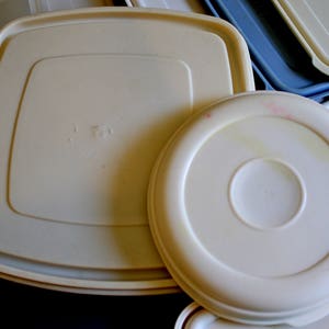 May include: Three white plastic storage containers with lids. The lids are slightly domed and have a smooth, glossy finish. The containers are stacked on top of each other.