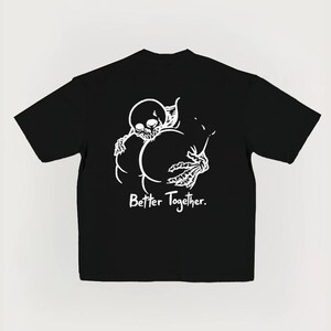 Puede incluir: Camiseta negra con un gr&aacute;fico blanco de un esqueleto abrazando dos formas redondeadas. El texto "Better Together" est&aacute; impreso debajo. La camiseta tiene mangas cortas y cuello redondo. El dise&ntilde;o es simple y audaz.
